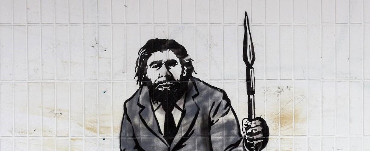 Luova seinämaalaus, jossa neandertalinihminen on puvussa ja pitelee toisessa kädessään keihästä.